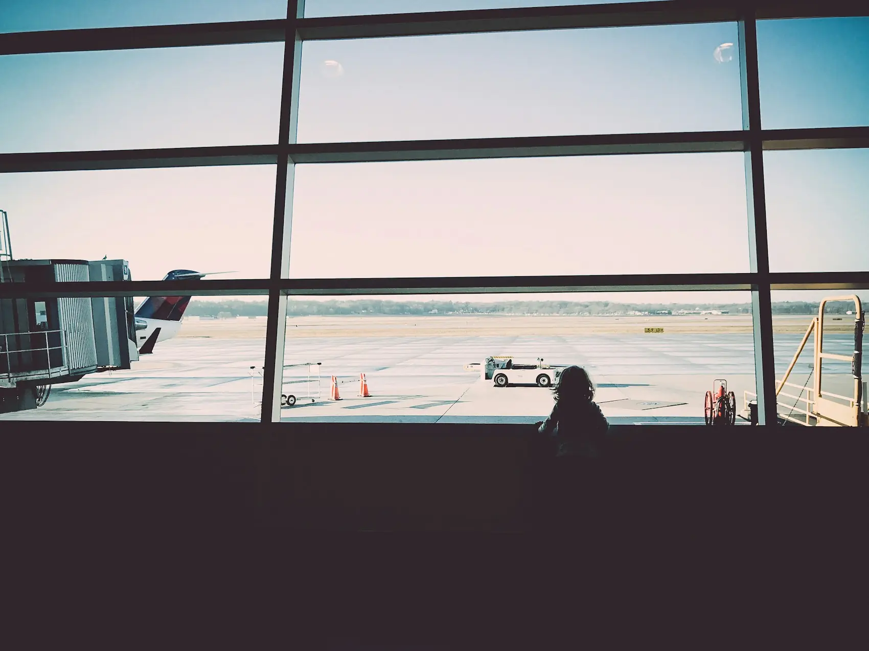 A traveler waiting by a wide airport window with planes on the tarmac